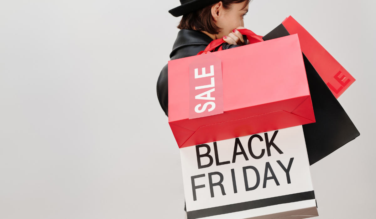 Red shopping bag with sale written on it. White shopping back with Black Friday on it. Carried by girl wearing a hat. 