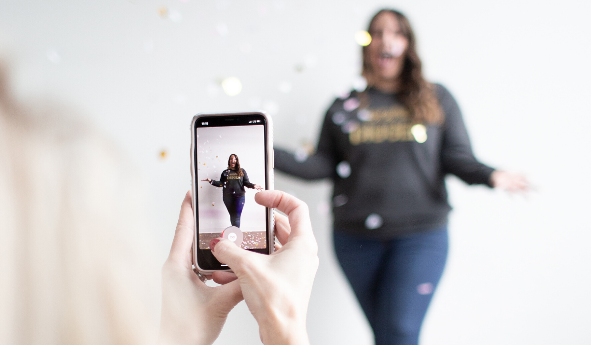 Taking a photo of a girl in a sweater and jeans with a mobile phone