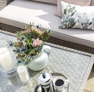 The Garden House candles, vases on an outdoor table in the sun with a floral cushion on outdoor seating