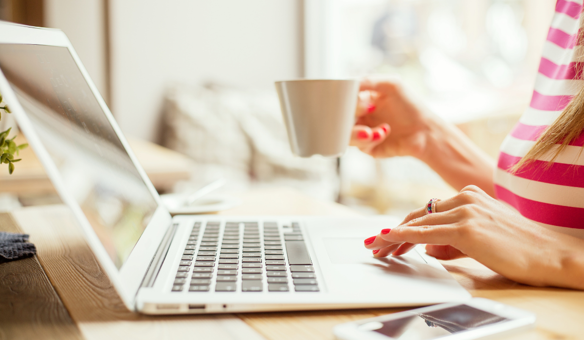 Female hand holding cup of coffee tea scrolling on white laptop