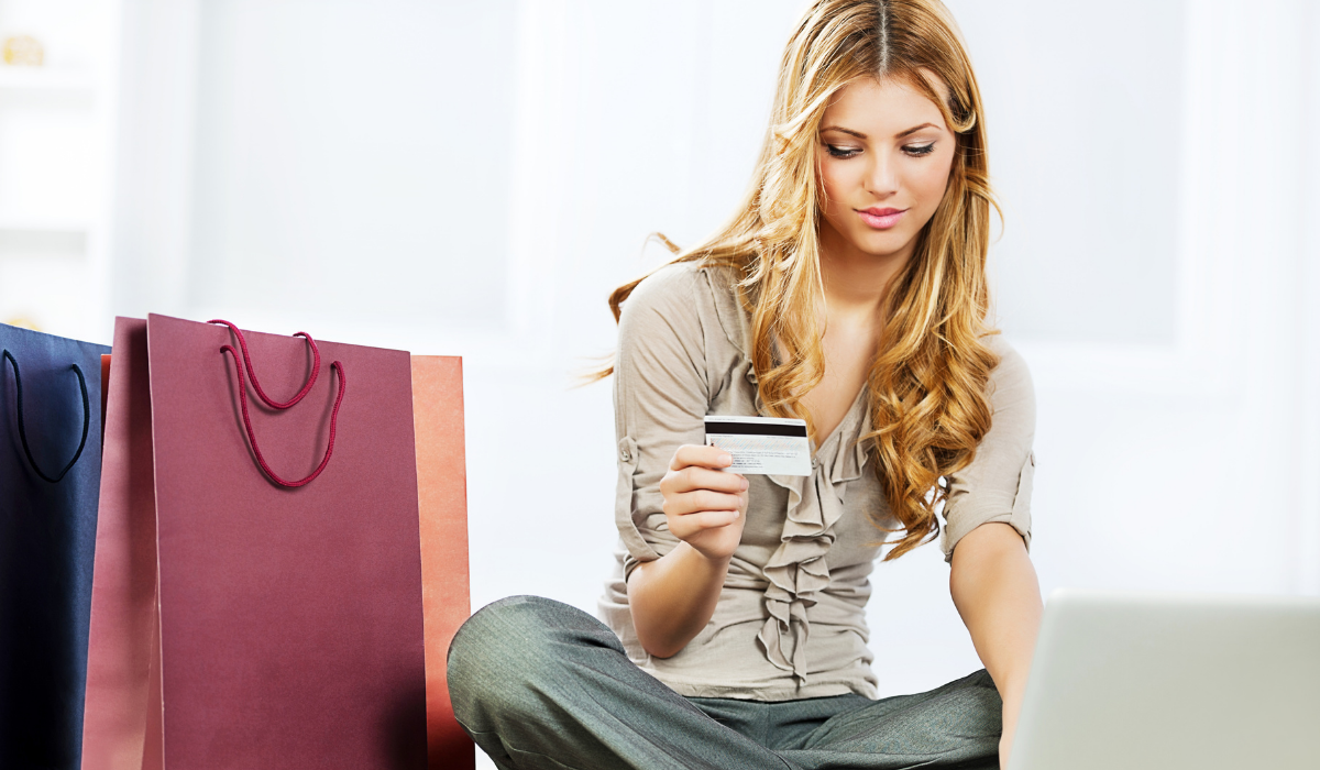 Image of girl with credit card sitting at a laptop surrounded by shopping bags. For article about key ecommerce shopping dates for 2021