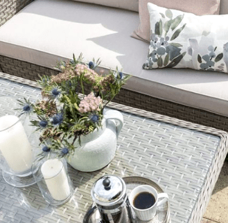The Garden House candles, vases on an outdoor table in the sun with a floral cushion on outdoor seating